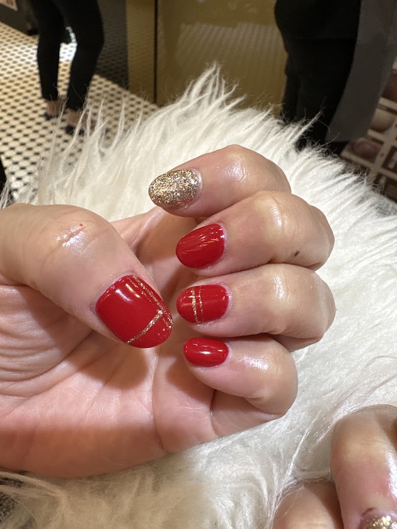 A hand displays freshly manicured nails with vibrant red polish, gold glitter, and delicate gold line art.