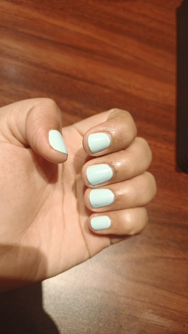 A hand showcasing light blue nail polish against a warm wooden background.
