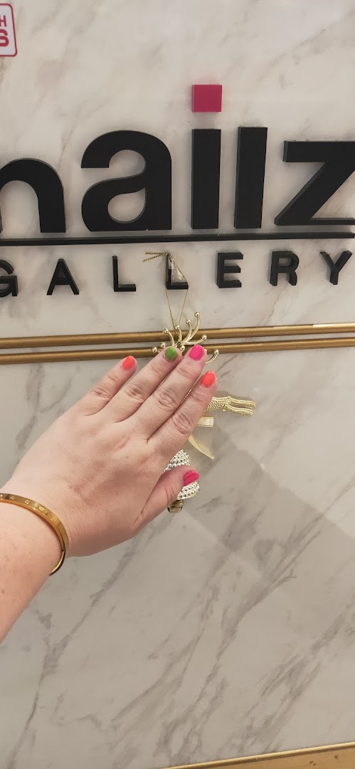 A hand with vibrant, multi-colored nails in front of the Nailz Gallery sign.