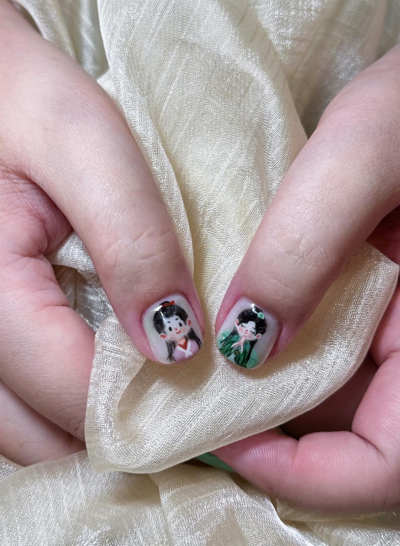 Close-up of hands showcasing intricate character nail art designs on two fingernails.