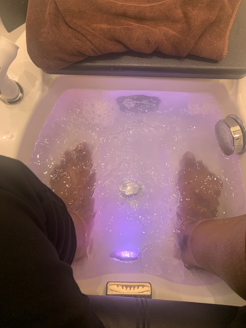 Feet soaking in a bubbling foot spa with purple light at Nailz Gallery.