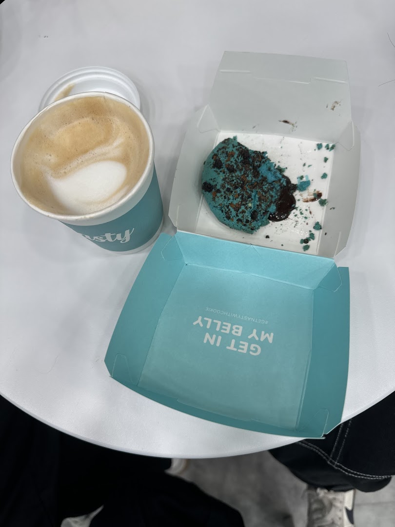 A partially eaten blue cookie in a box with a coffee cup on a white table.