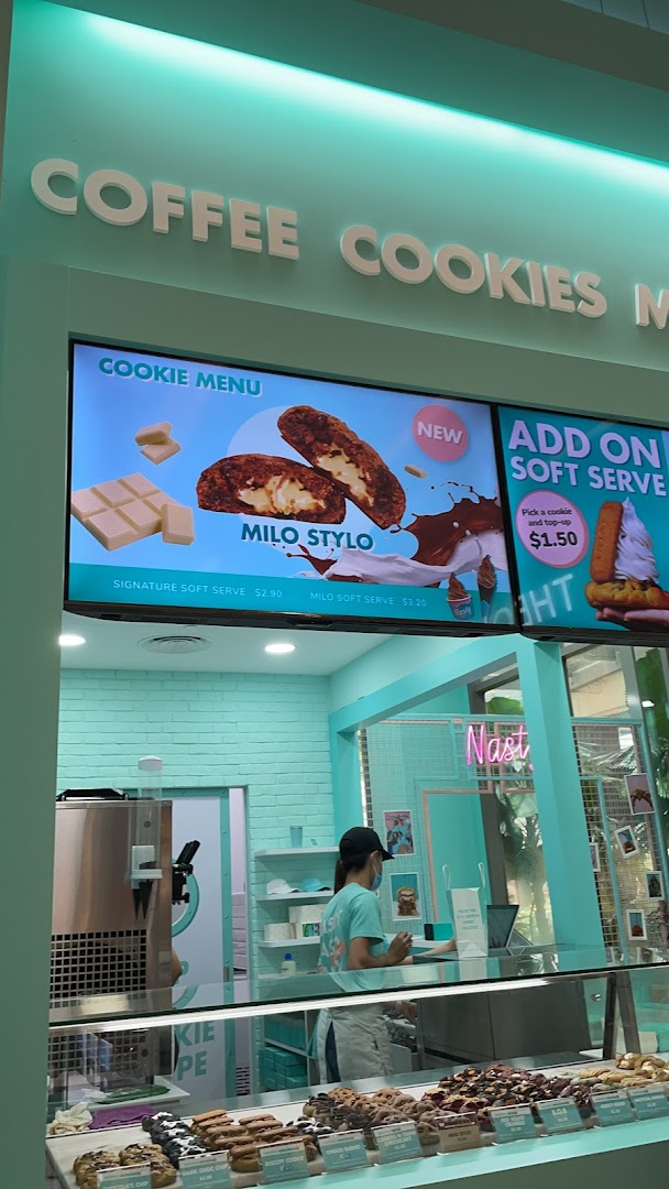 Interior view of Nasty Cookie - Westgate, showcasing the counter, staff, and digital menu boards.