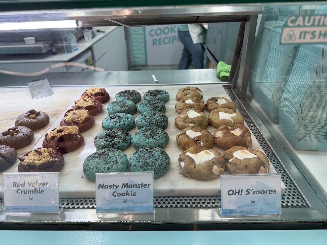 A vibrant display of gourmet cookies, including Red Velvet Crumble, Nasty Monster, and OH! S'mores.