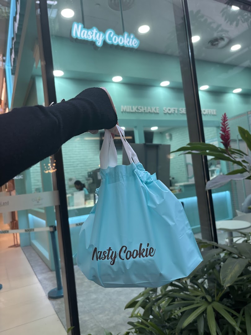 A person holds a Nasty Cookie bag outside the shop's teal-themed entrance.