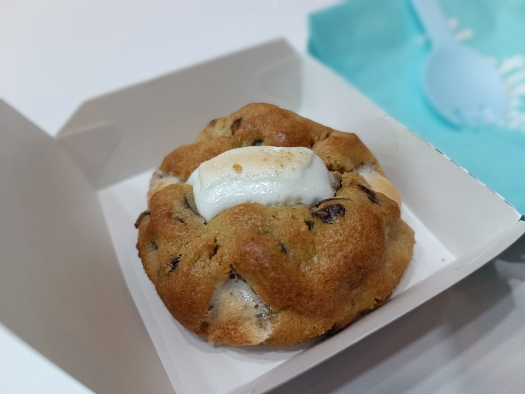 A close-up of a delicious chocolate chip cookie with a melted marshmallow center in a white box.