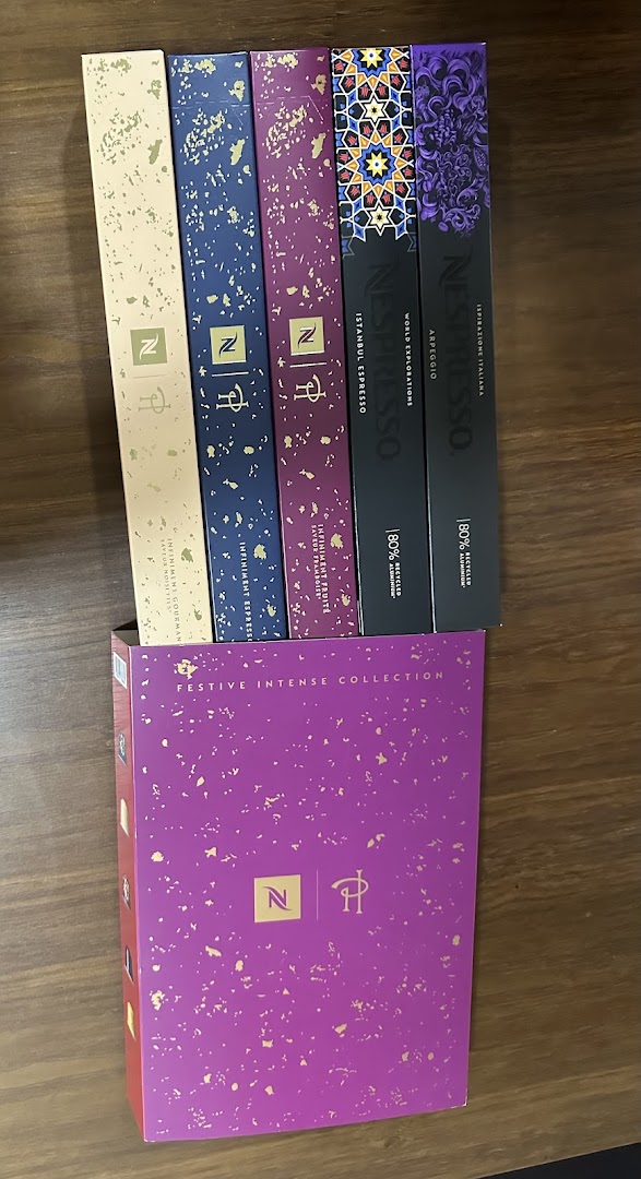 A vibrant display of Nespresso coffee capsule boxes, including a 'Festive Intense Collection' gift set.