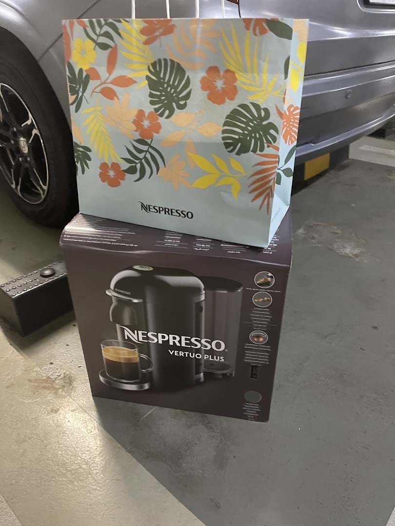 A Nespresso Vertuo Plus machine box topped with a tropical-themed Nespresso shopping bag.