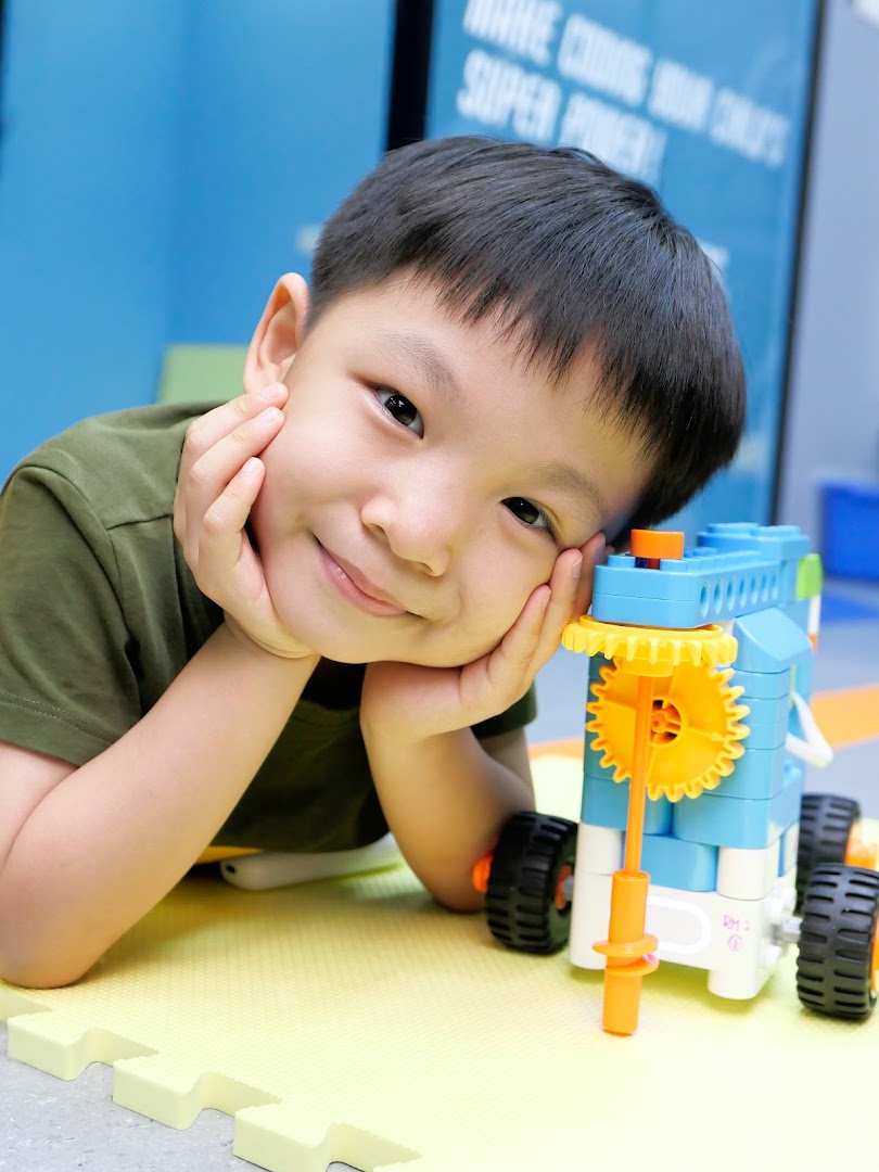 A happy child smiles while engaging with a robotics kit on a soft play mat at NK Robotics.