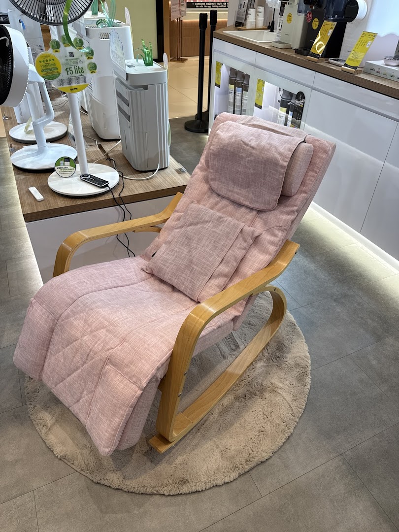 A comfortable pink massage chair on a round rug, displayed in a retail setting with other home appliances.