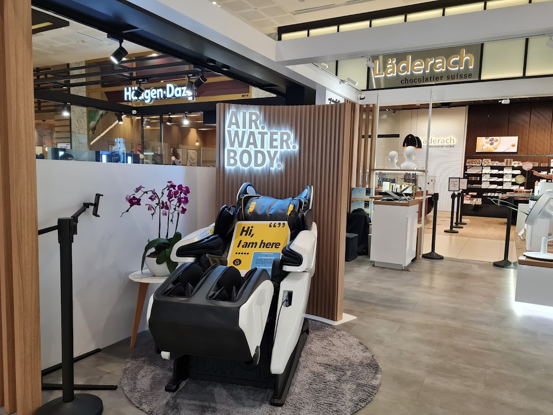 A modern massage chair display with a 'AIR. WATER. BODY.' sign, set within a shopping mall environment.