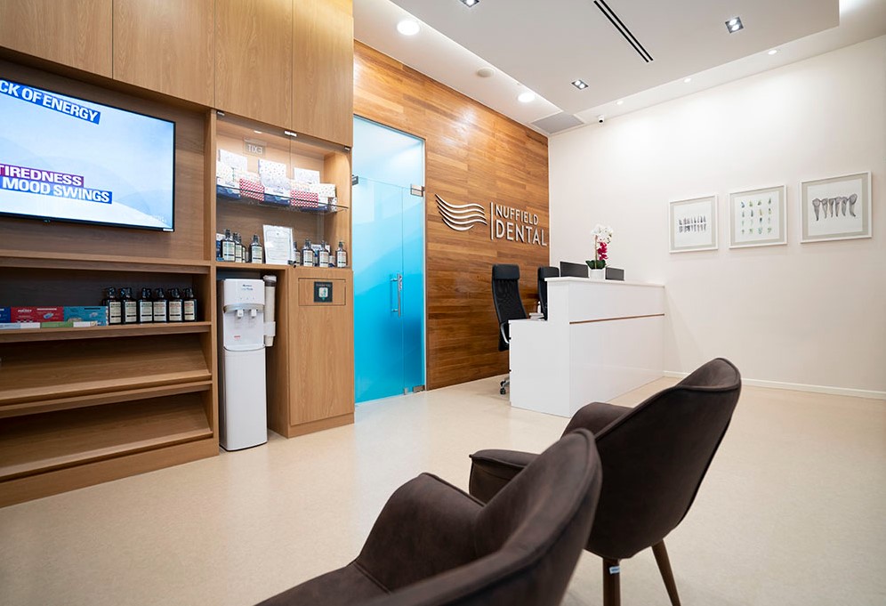 A modern and inviting dental clinic waiting area with a reception desk, comfortable seating, and branded wall.