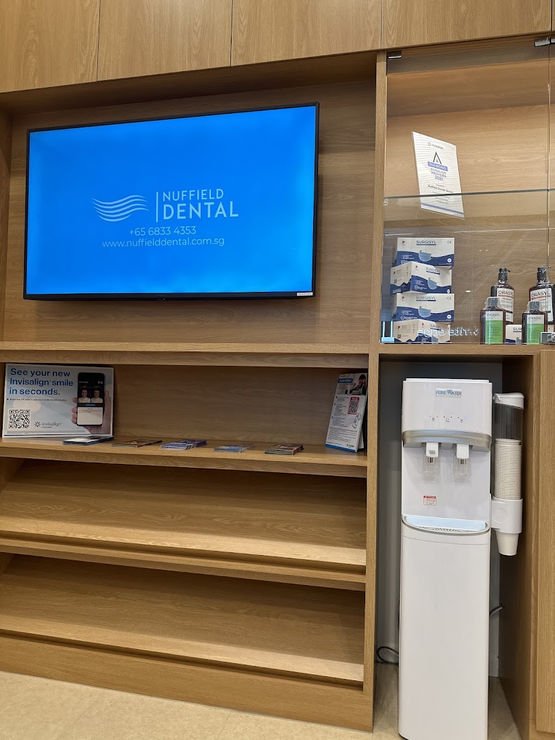 Interior view of Nuffield Dental's waiting area with a branding screen, shelves, and water dispenser.