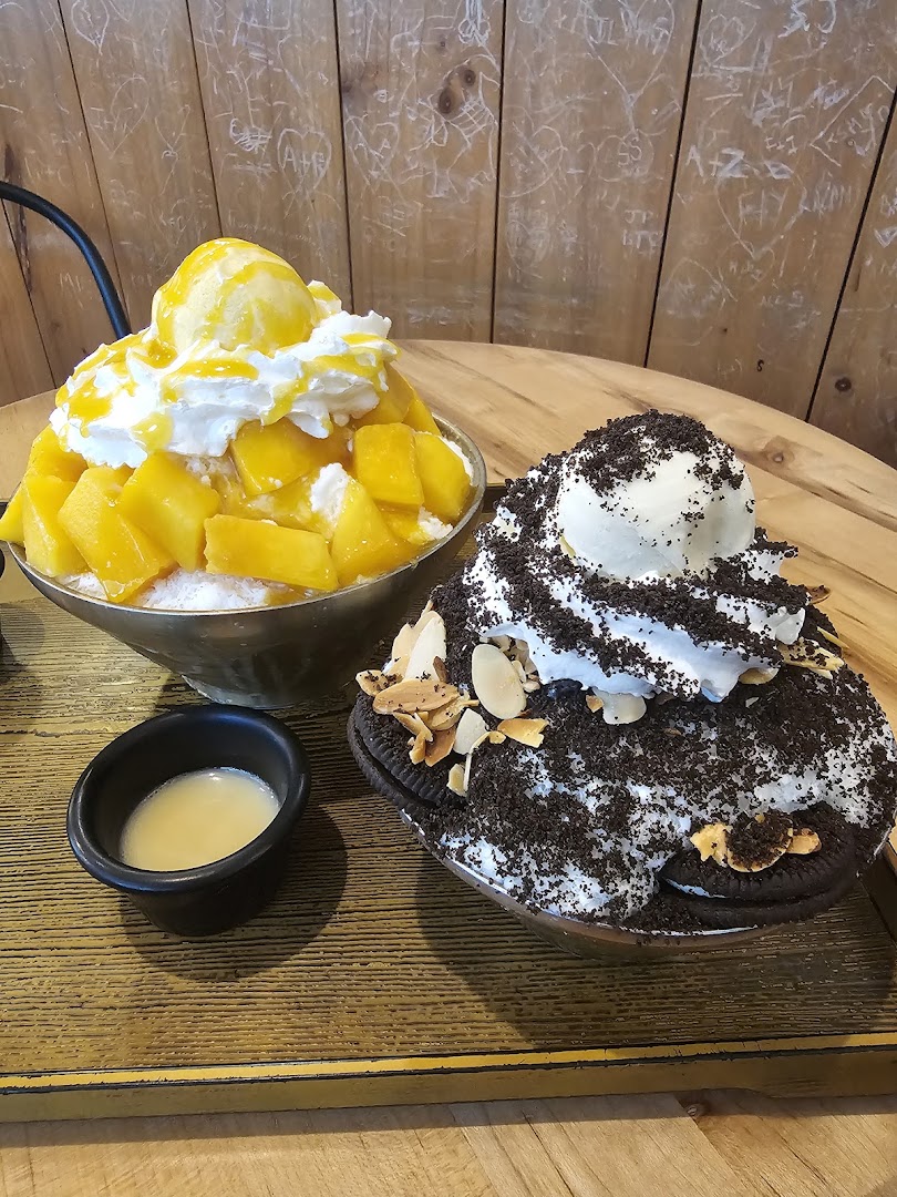Two delicious Korean shaved ice desserts, mango and chocolate, served on a wooden tray.