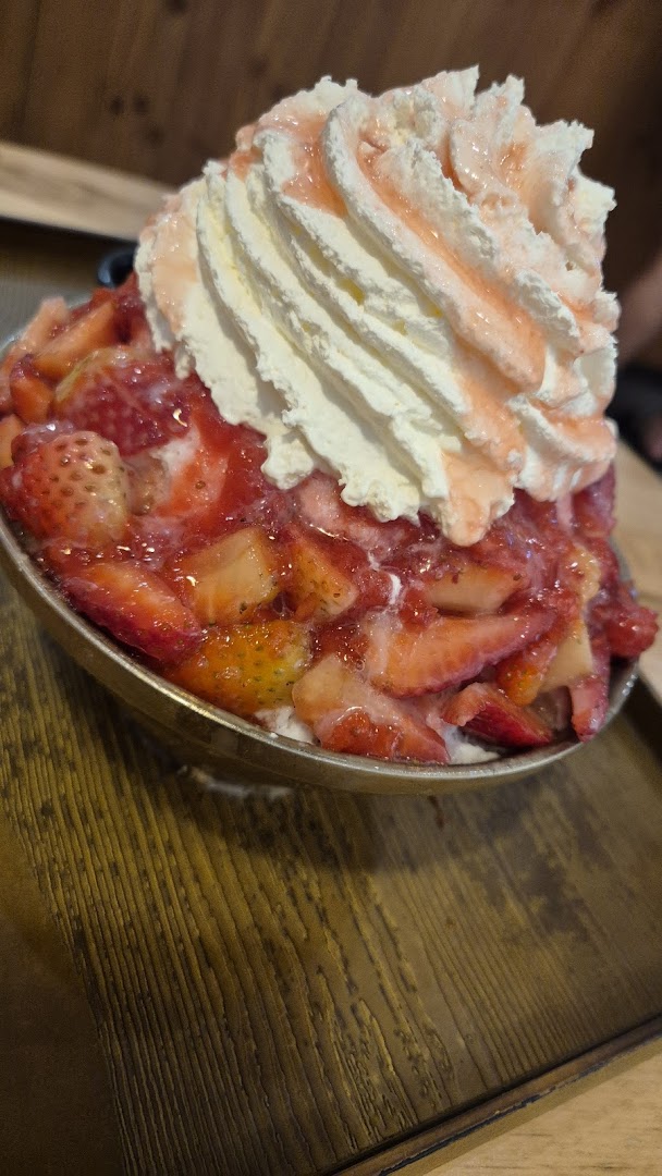 A close-up of a large bowl of strawberry bingsu topped with whipped cream and strawberry syrup.