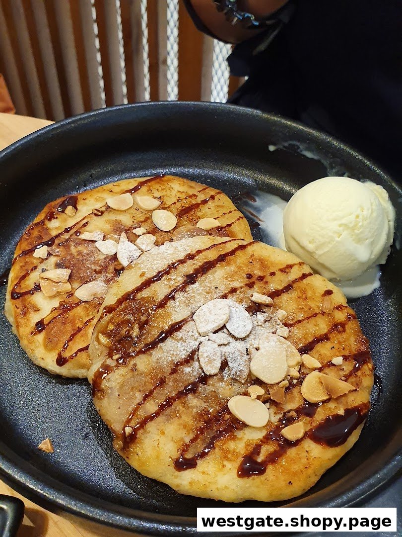 Two golden pancakes topped with chocolate drizzle, almond slivers, and powdered sugar, served with vanilla ice cream.