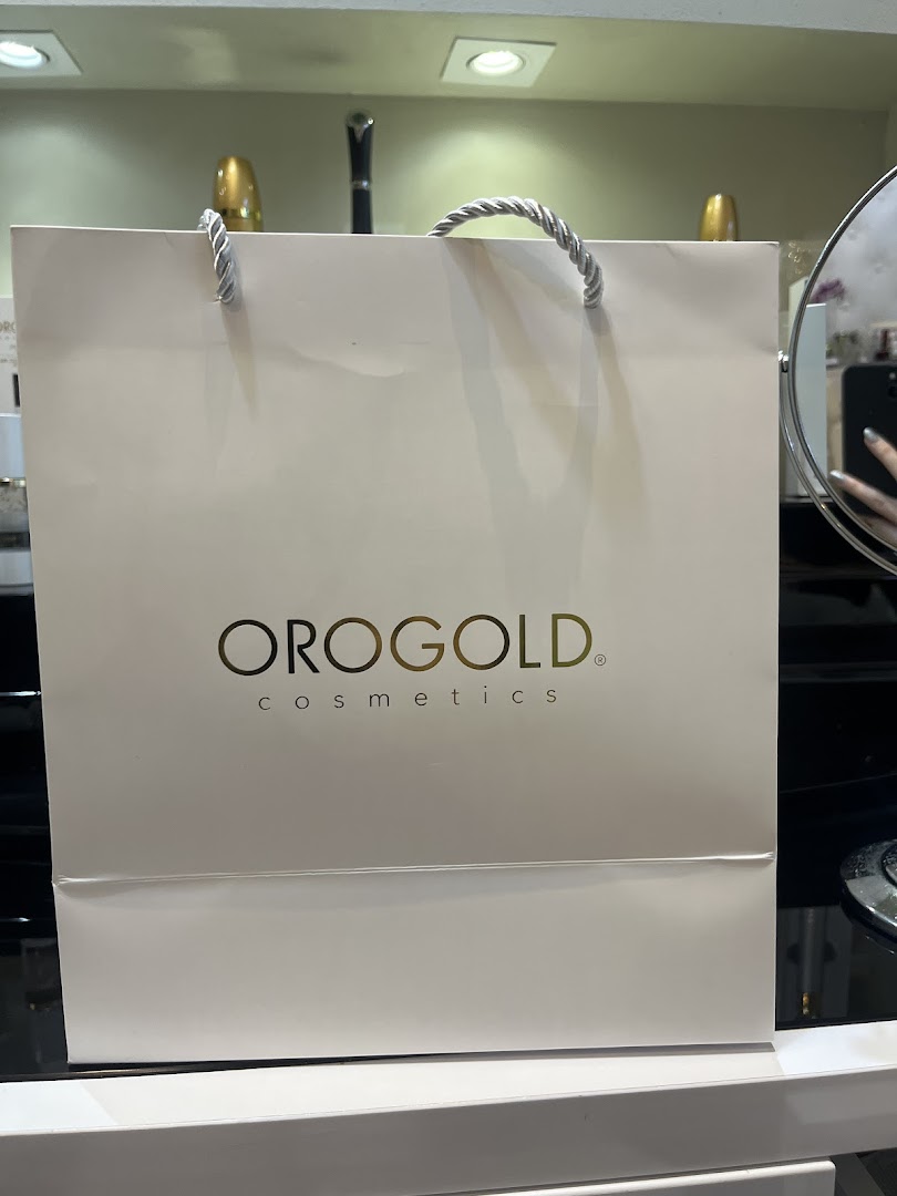 A white OROGOLD Cosmetics shopping bag with gold logo and silver handles.