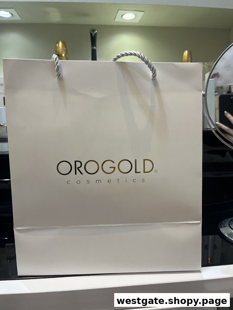 A white OROGOLD Cosmetics shopping bag with gold logo and silver handles.