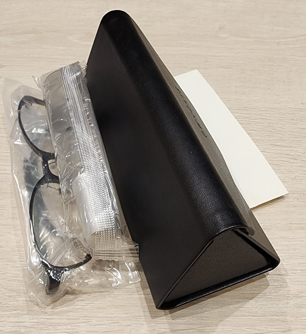 A new pair of eyeglasses in packaging with a case and cleaning cloth on a wooden surface.