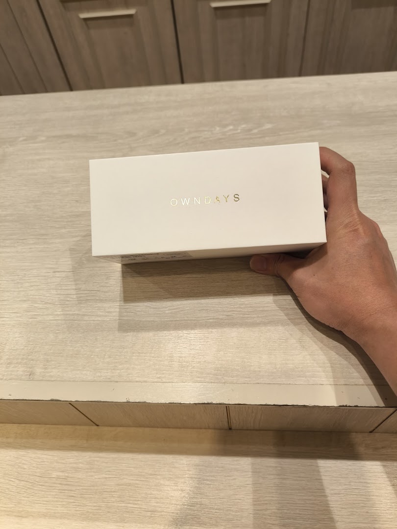 A hand holding a white OWNDAYS product box with gold lettering.