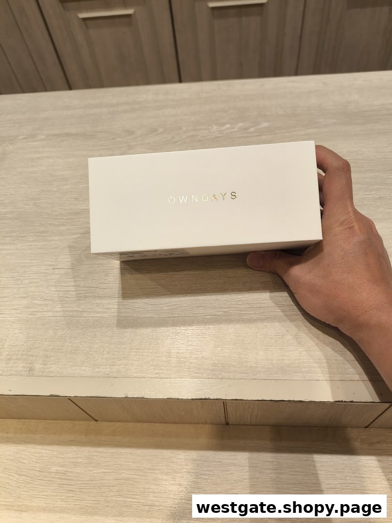 A hand holding a white OWNDAYS product box with gold lettering.