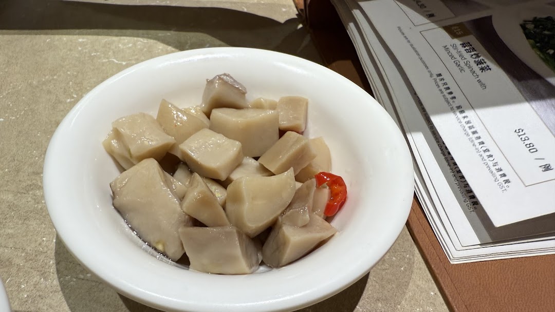 A bowl of braised cubed vegetables with a red chili, next to a menu displaying Stir-fried Spinach.
