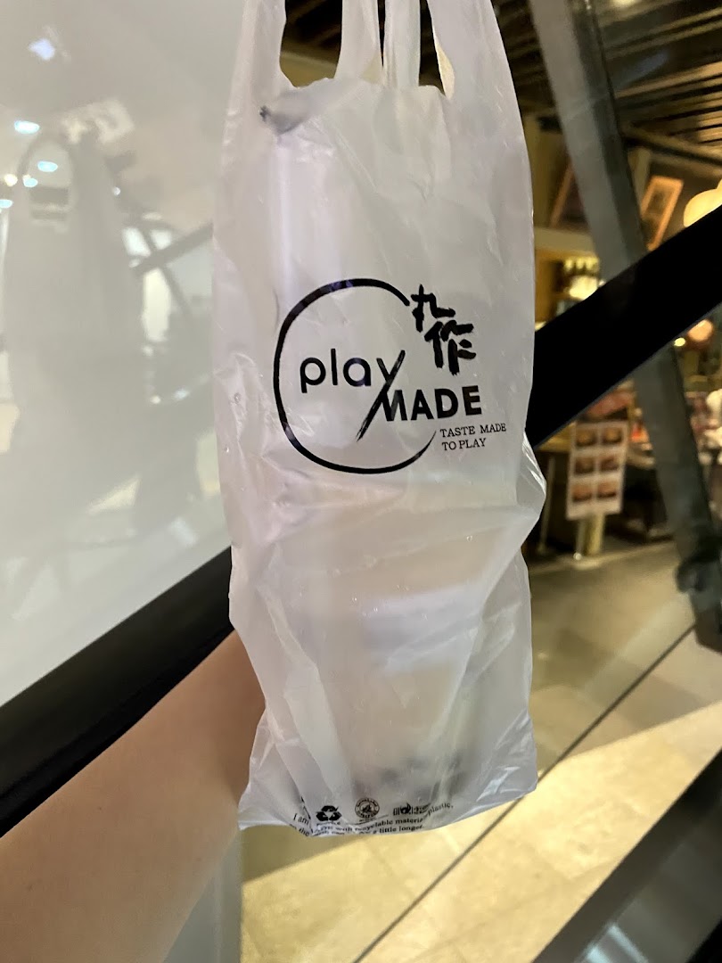A hand holds a PlayMade bubble tea drink in a branded plastic bag.