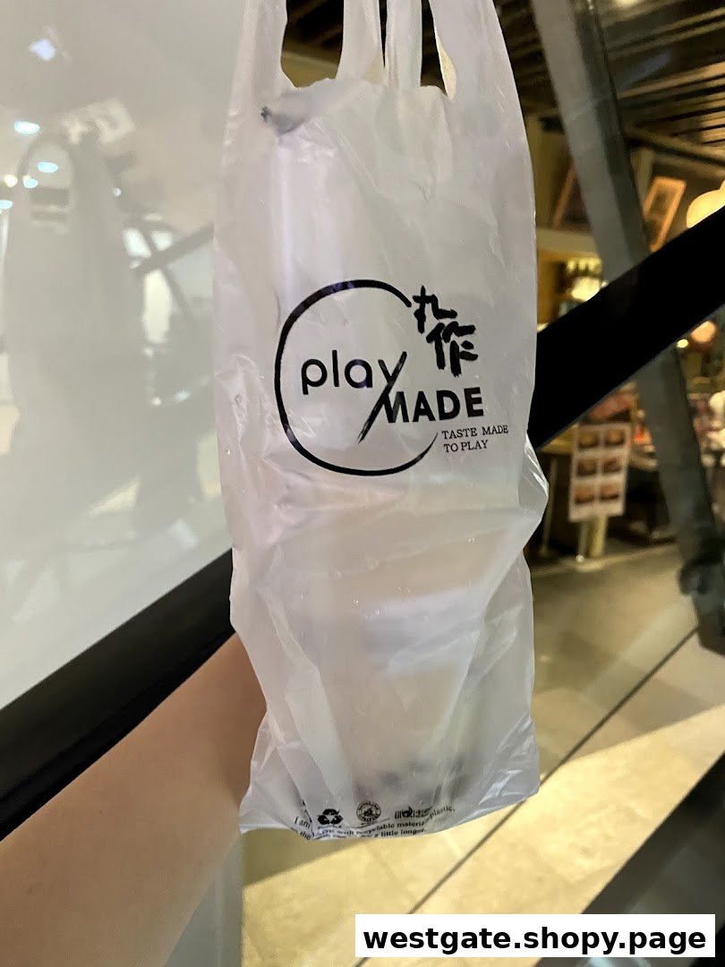 A hand holds a PlayMade bubble tea drink in a branded plastic bag.