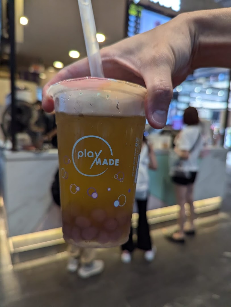 A hand holds a refreshing PlayMade bubble tea drink with purple pearls, showcasing the brand logo.
