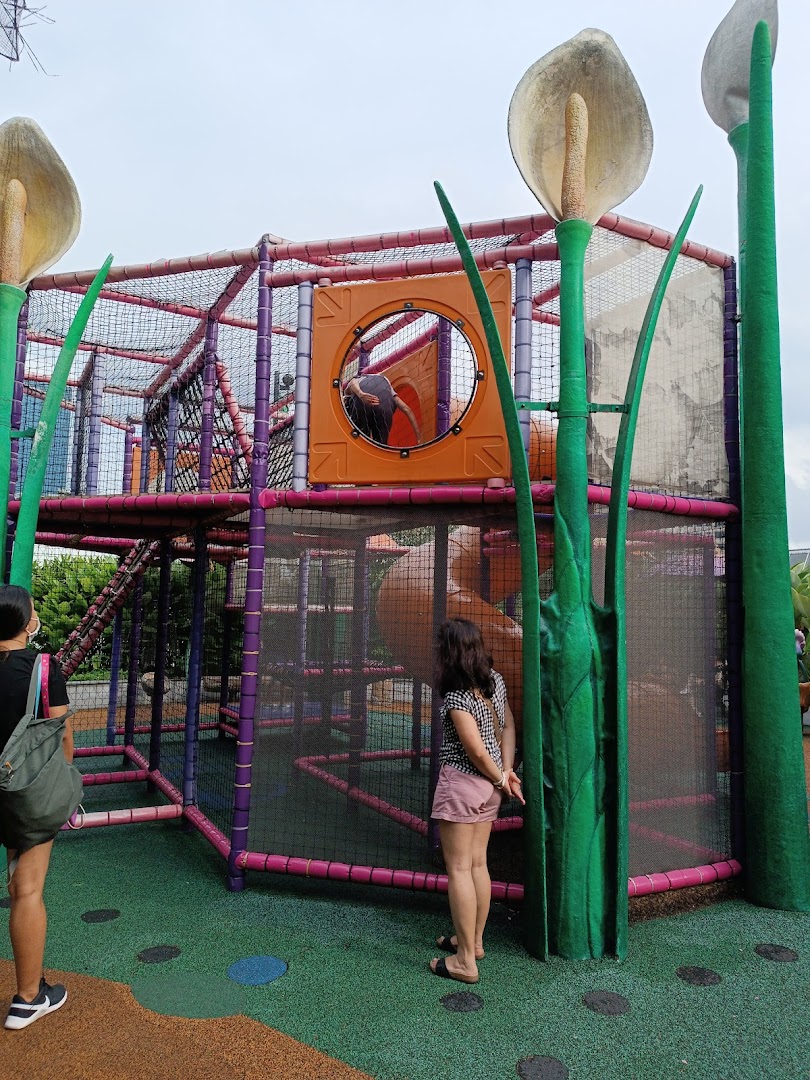 A vibrant outdoor playground with a large climbing structure and two adults observing.