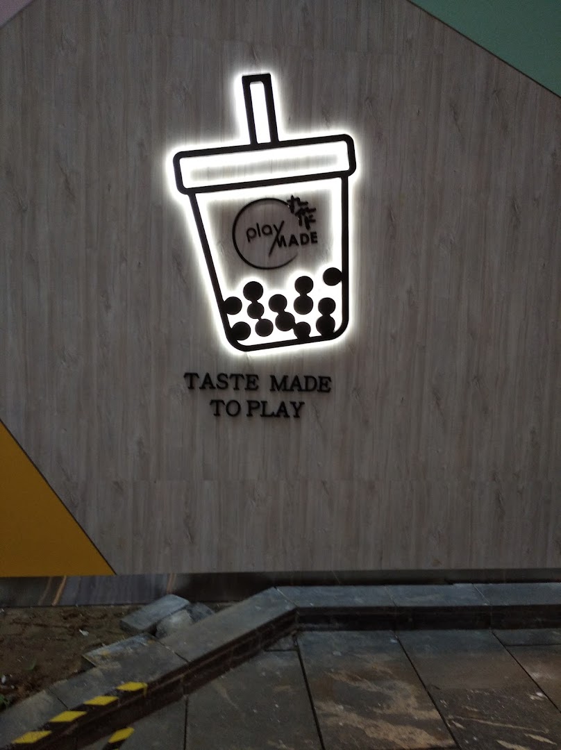 Illuminated PlayMade bubble tea logo and 'Taste Made to Play' slogan on a textured wall.