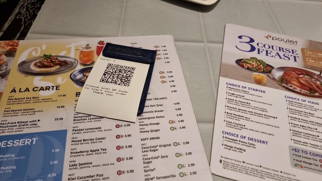 Close-up view of Poulet restaurant menus on a table, featuring a QR code for ordering.