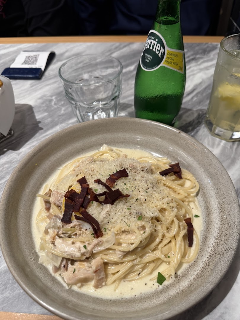 A creamy pasta dish with chicken and crispy toppings, served with Perrier and a refreshing drink.