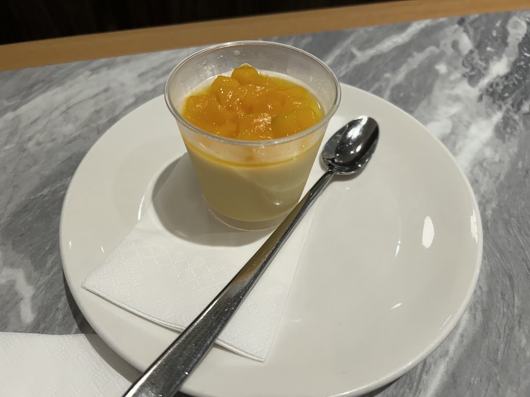 A creamy dessert topped with diced mango, served on a white plate with a spoon.