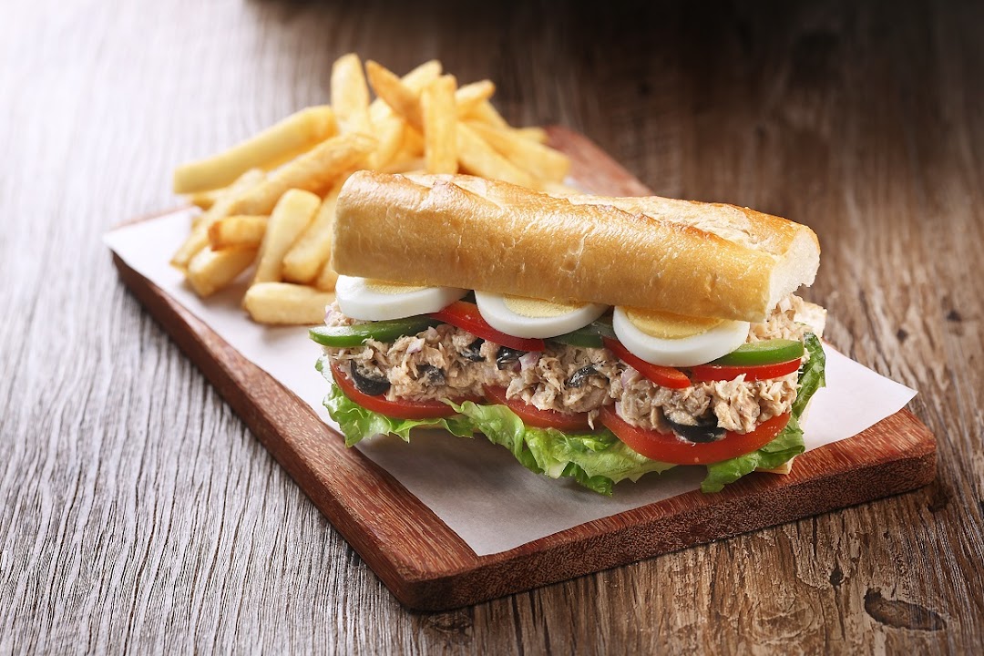 A delicious tuna baguette sandwich with hard-boiled eggs and vegetables, served with golden french fries.