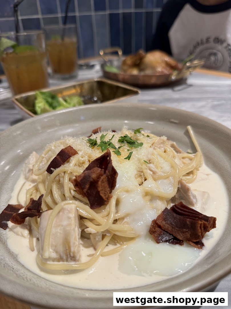 A close-up of creamy pasta with chicken, bacon, and a poached egg, with drinks and roasted chicken in the background.
