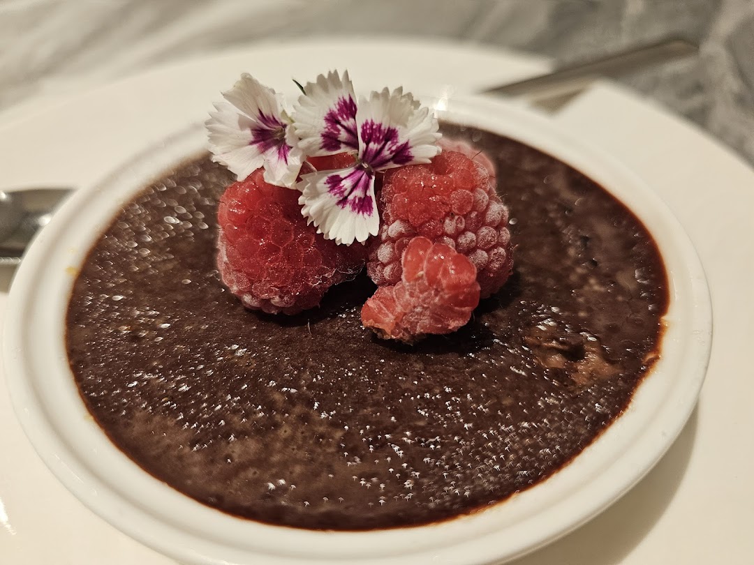 A rich chocolate dessert garnished with fresh raspberries and delicate edible flowers, served in a white ramekin.