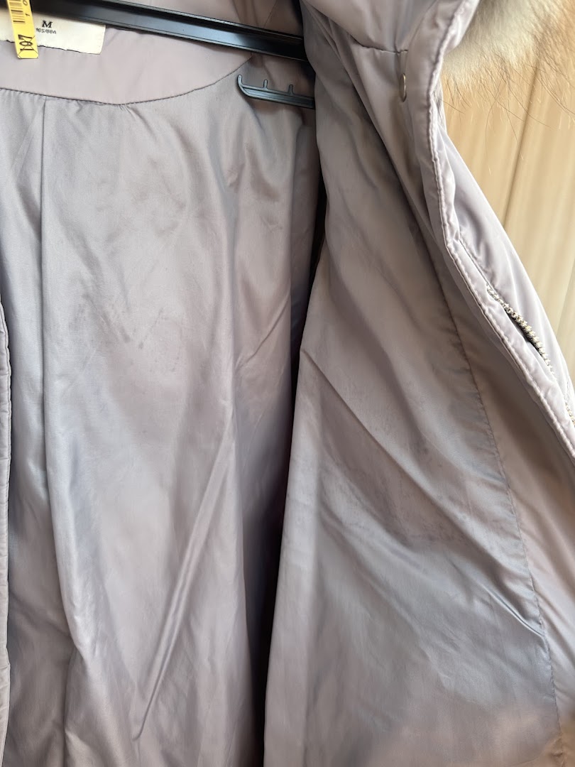 Close-up of the inside of a light-colored coat, likely after professional dry cleaning, with a tag visible.