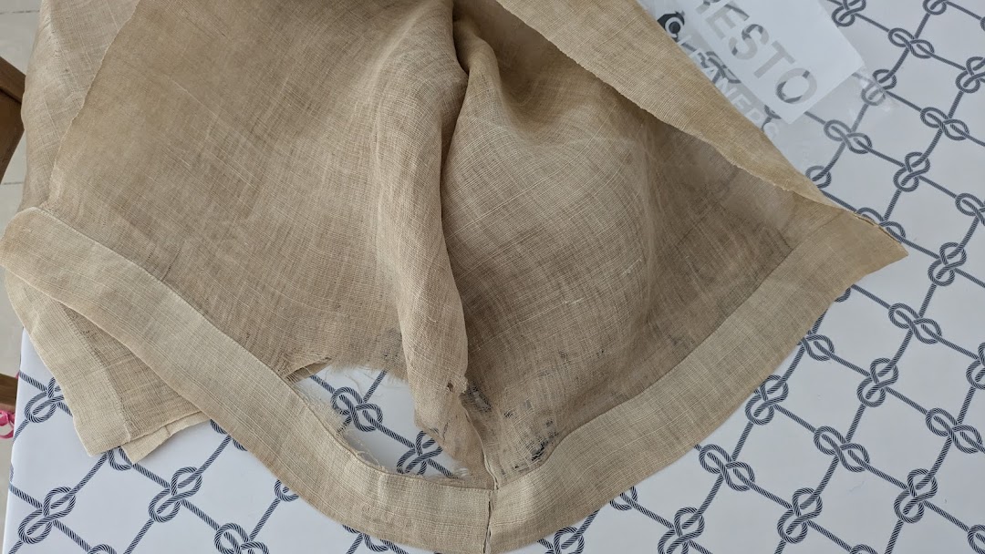 A piece of light brown fabric, possibly linen, on a patterned surface with the Presto Drycleaners logo visible.