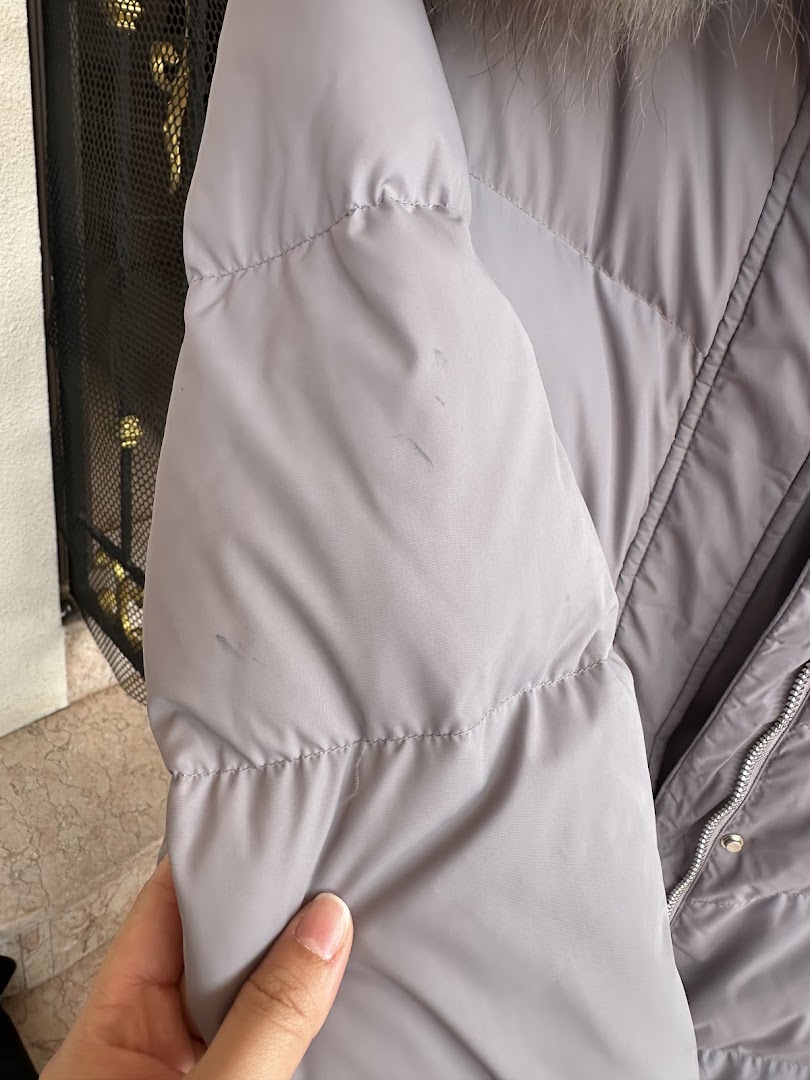 Close-up of a grey puffer jacket with visible stains, held by a hand.