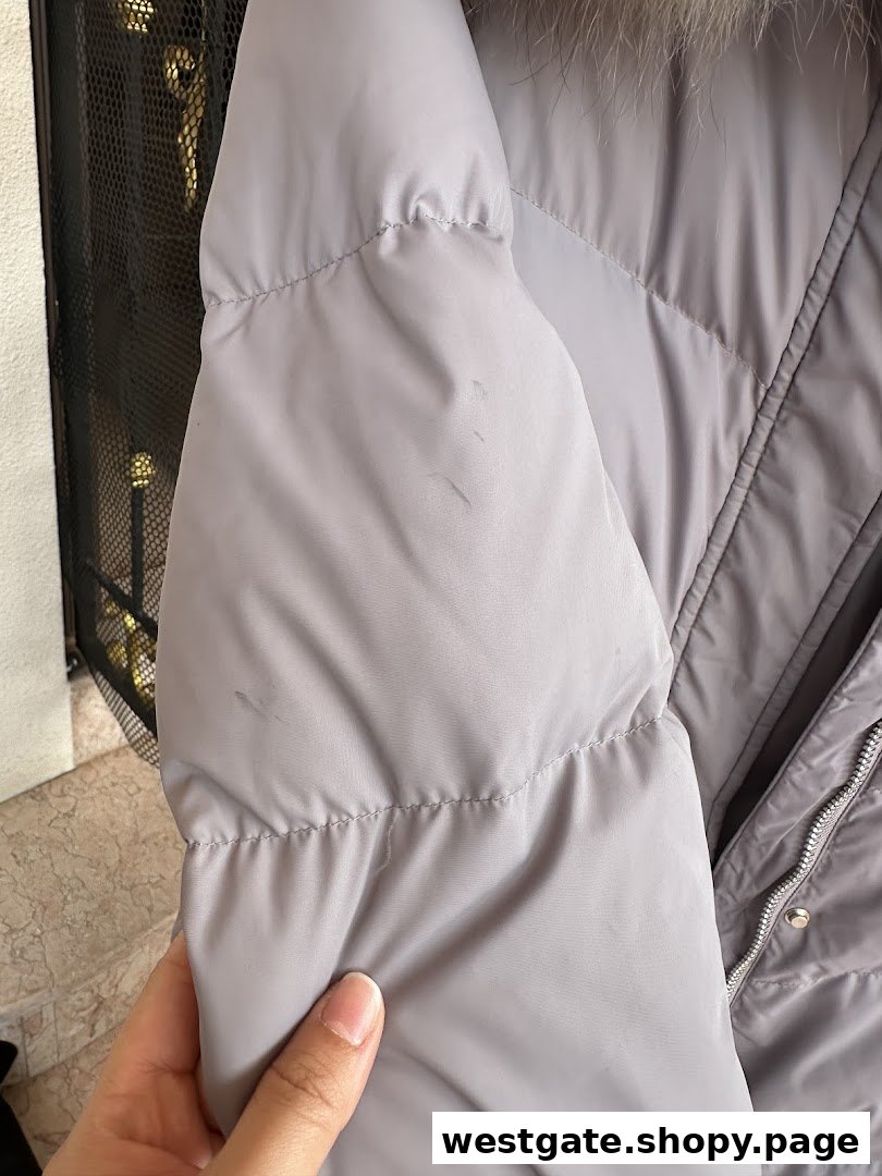 Close-up of a grey puffer jacket with visible stains, held by a hand.