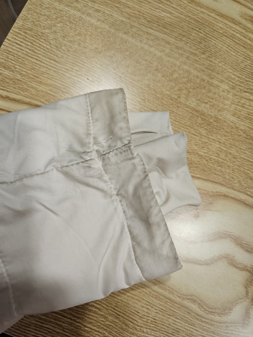 Close-up of a dirty, light-colored garment sleeve on a wooden surface, showing wear and stains.