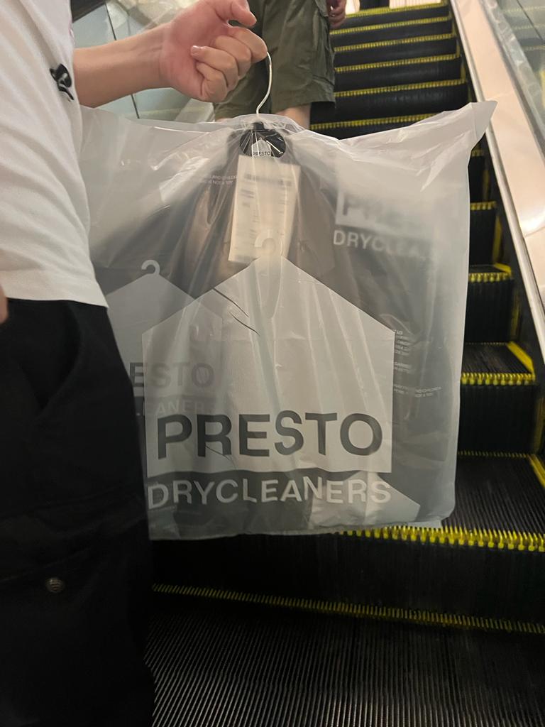 A person carries a freshly dry-cleaned garment in a Presto Drycleaners bag on an escalator.