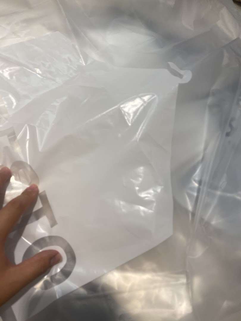 A hand holds a white plastic garment bag, likely from a dry cleaner, showing part of a logo.