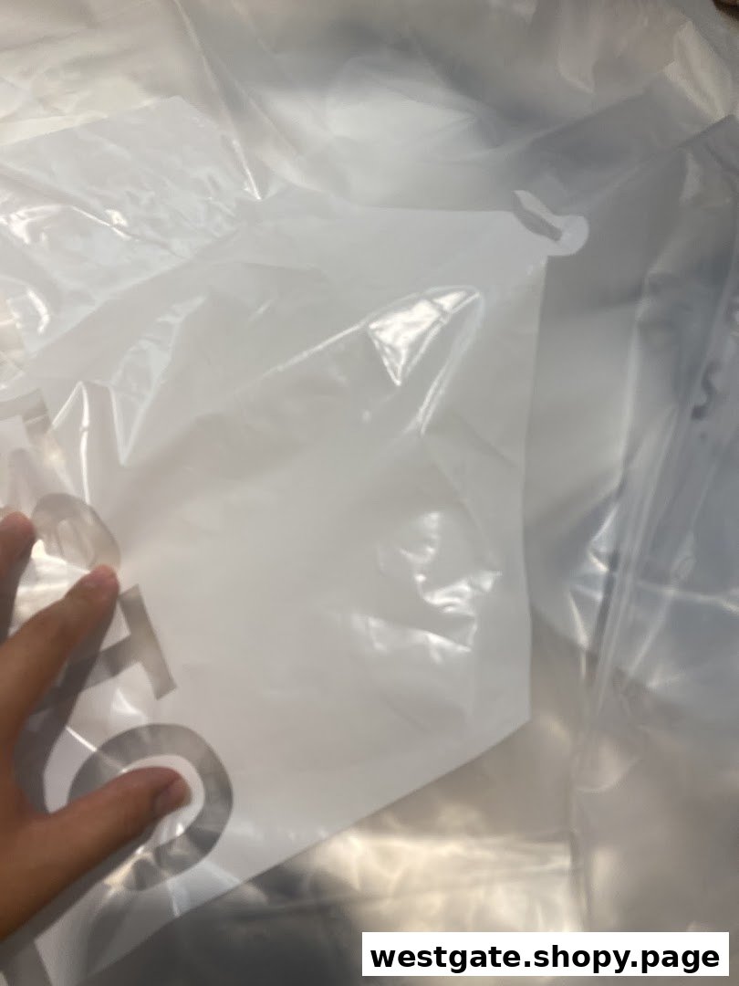 A hand holds a white plastic garment bag, likely from a dry cleaner, showing part of a logo.