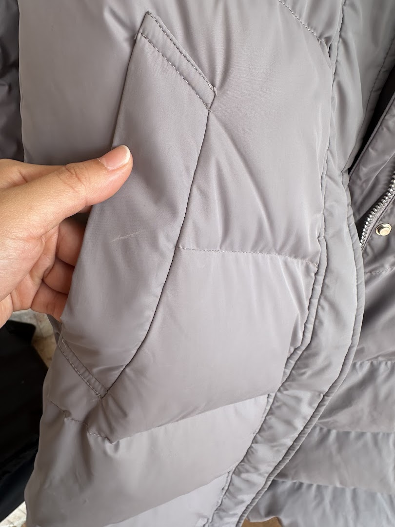 Close-up of a grey puffer jacket with a small mark, being inspected by a hand.