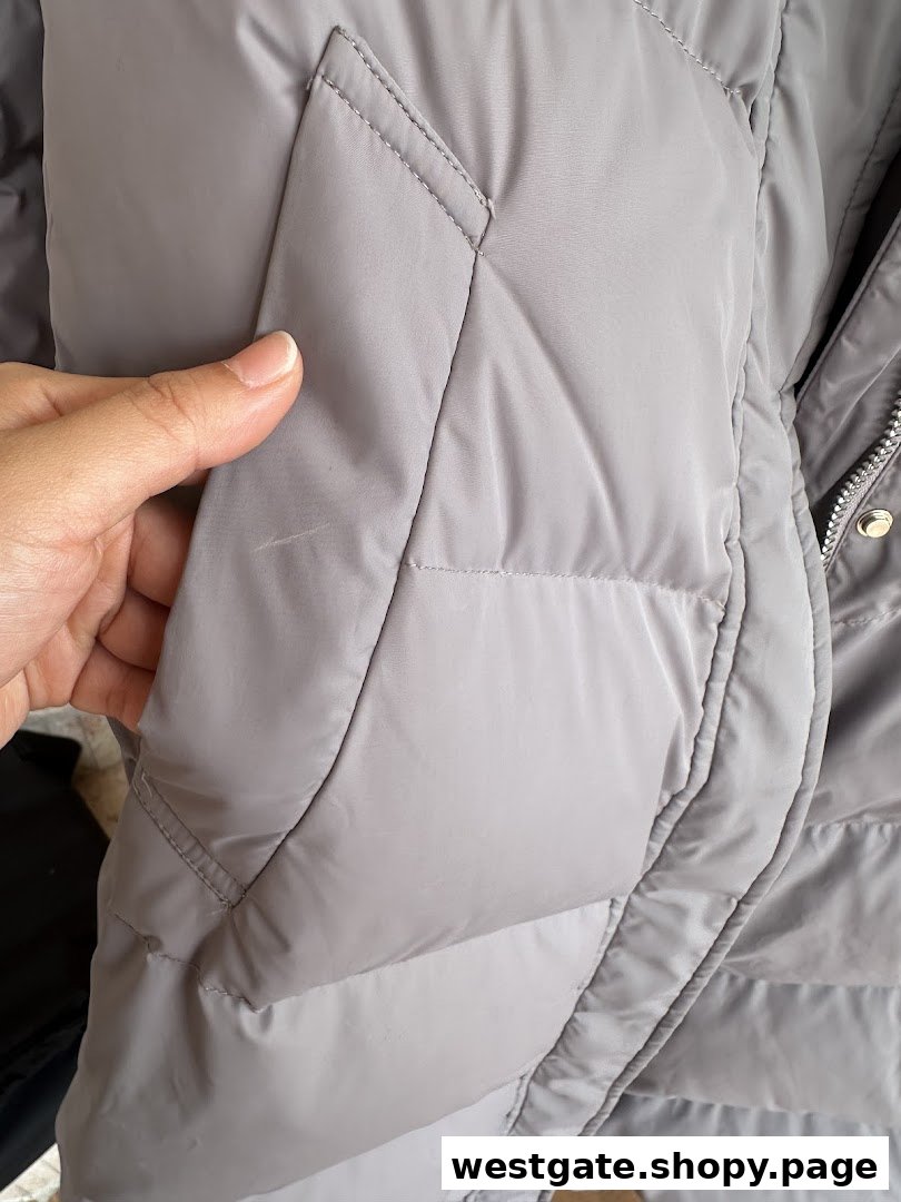 Close-up of a grey puffer jacket with a small mark, being inspected by a hand.