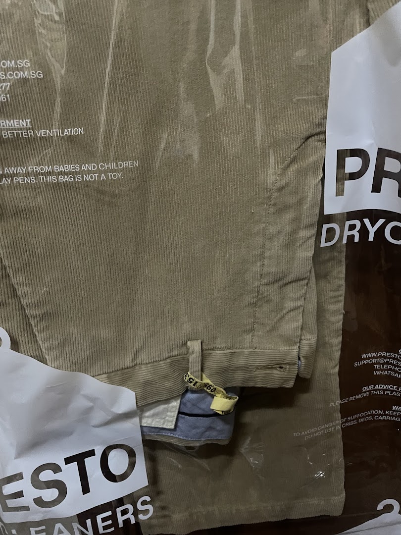 A pair of freshly dry-cleaned corduroy trousers in a clear plastic bag from Presto Drycleaners.