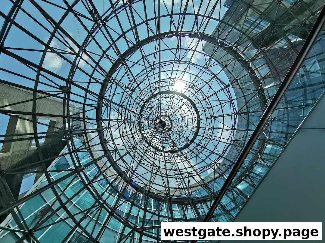 View looking up into a modern glass and steel dome atrium with bright sky.