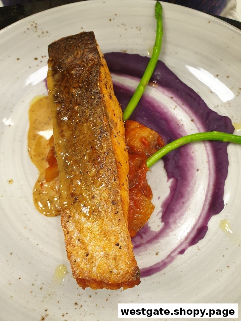 A gourmet dish featuring pan-seared salmon with purple puree, asparagus, and a rich sauce.